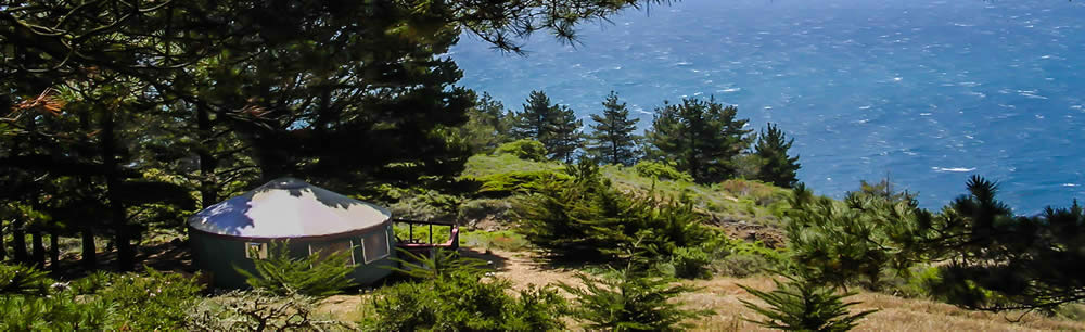 Round white yurt in trees overlooking coast